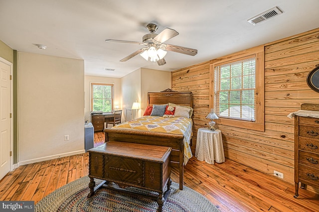 bedroom with ceiling fan, light hardwood / wood-style floors, and wood walls