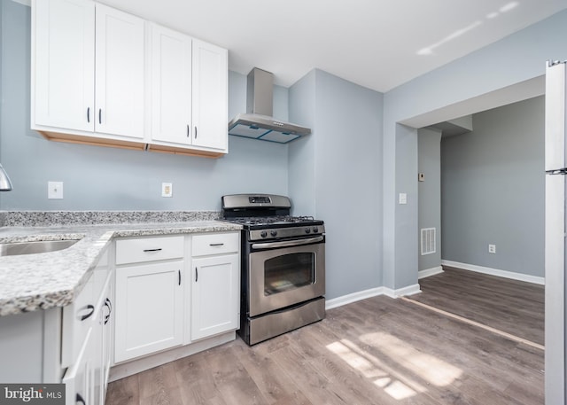 kitchen with white cabinets, stainless steel gas range oven, wall chimney range hood, and light hardwood / wood-style floors