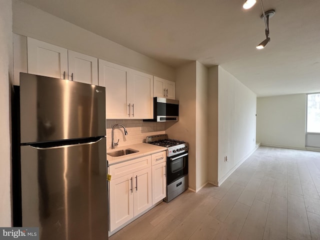 kitchen with light hardwood / wood-style floors, decorative backsplash, sink, appliances with stainless steel finishes, and white cabinets