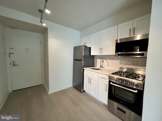 kitchen with white cabinets, stainless steel appliances, sink, backsplash, and light wood-type flooring