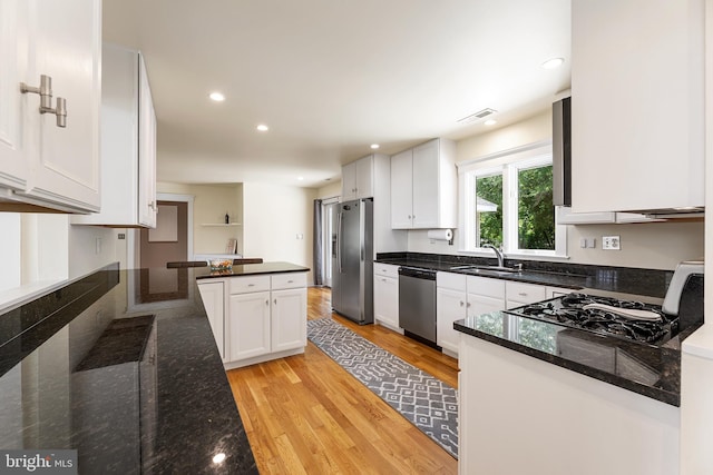 kitchen with appliances with stainless steel finishes, light wood-type flooring, dark stone counters, sink, and white cabinetry