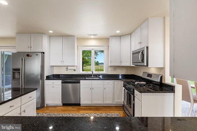 kitchen featuring white cabinets, appliances with stainless steel finishes, dark stone counters, and sink