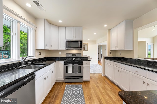 kitchen featuring white cabinetry, sink, dark stone countertops, light hardwood / wood-style floors, and appliances with stainless steel finishes