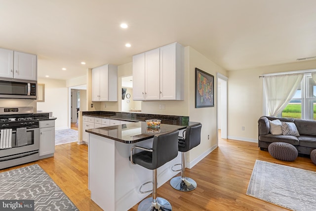 kitchen with white cabinets, light hardwood / wood-style flooring, dark stone countertops, a kitchen bar, and stainless steel appliances