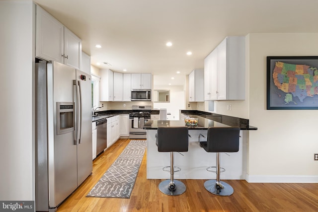 kitchen featuring white cabinets, appliances with stainless steel finishes, light wood-type flooring, and a kitchen breakfast bar