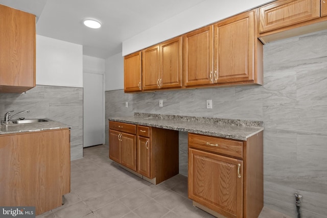 kitchen featuring backsplash, sink, light stone countertops, and light tile flooring