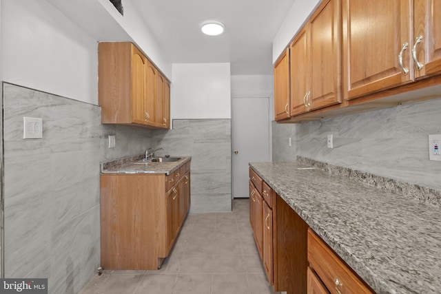 kitchen featuring tile walls, light stone counters, sink, and light tile floors