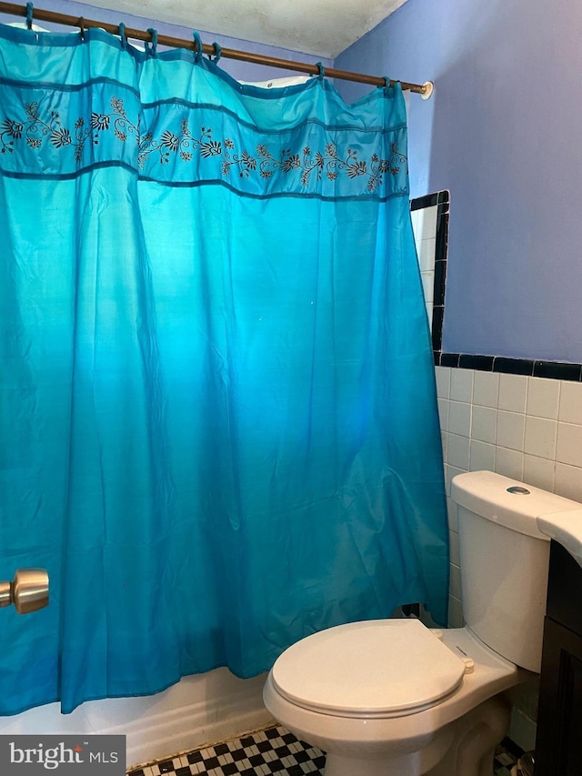 bathroom with toilet, wainscoting, tile walls, and shower / tub combo with curtain