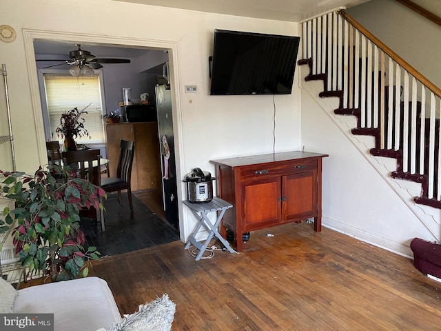 living area with stairway, wood-type flooring, and a ceiling fan