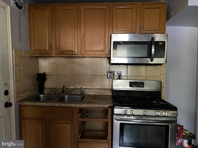 kitchen with stainless steel appliances, a sink, tasteful backsplash, brown cabinetry, and dark countertops