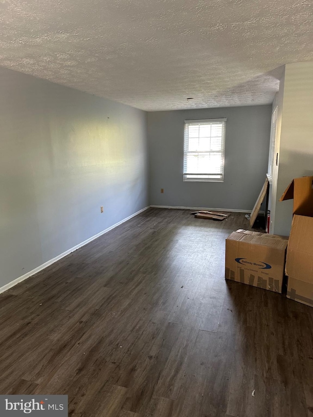 empty room with dark wood finished floors, a textured ceiling, and baseboards