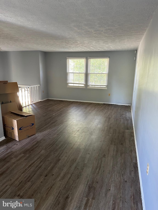 unfurnished living room featuring dark wood finished floors, a textured ceiling, and baseboards