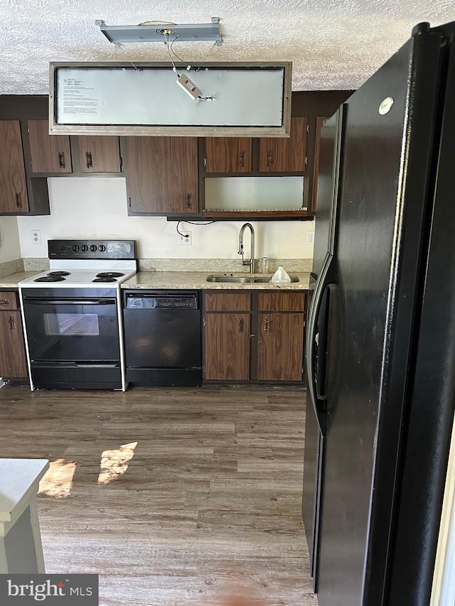 kitchen with black appliances, wood finished floors, a sink, and light countertops