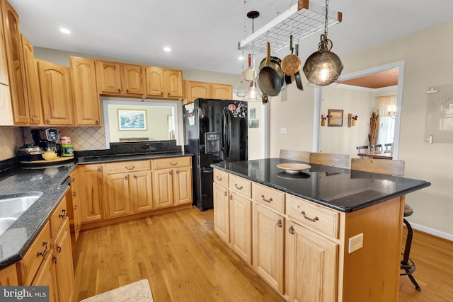 kitchen featuring a center island, black fridge, light hardwood / wood-style floors, decorative light fixtures, and a breakfast bar