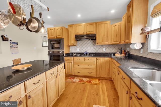 kitchen with decorative backsplash, light brown cabinets, light hardwood / wood-style floors, and dark stone counters