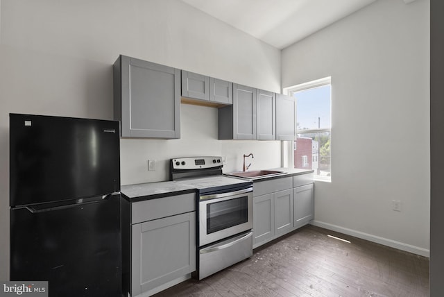 kitchen featuring stainless steel electric range oven, wood-type flooring, black refrigerator, gray cabinetry, and sink