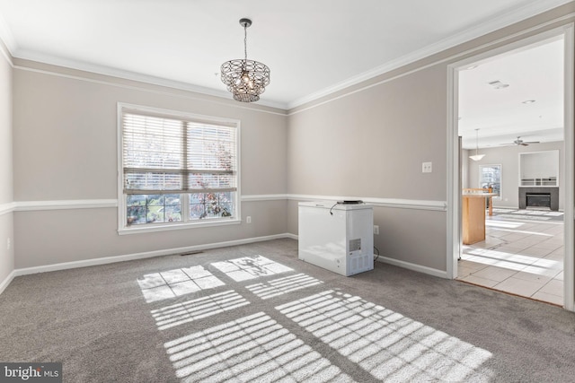 spare room with crown molding, carpet floors, a tile fireplace, and ceiling fan with notable chandelier