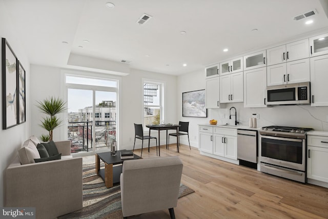 interior space featuring appliances with stainless steel finishes, white cabinets, backsplash, and light wood-type flooring