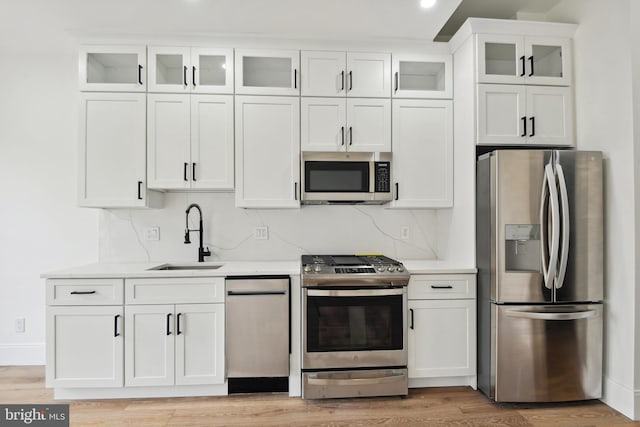 kitchen with white cabinets, light hardwood / wood-style floors, stainless steel appliances, backsplash, and sink