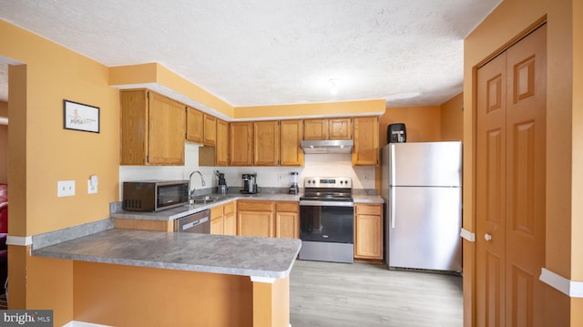 kitchen with kitchen peninsula, appliances with stainless steel finishes, a textured ceiling, sink, and light hardwood / wood-style floors