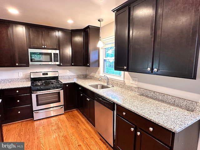 kitchen with sink, light hardwood / wood-style flooring, stainless steel appliances, decorative light fixtures, and light stone countertops