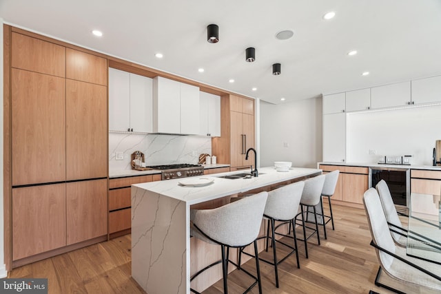 kitchen with white cabinets, a center island with sink, sink, and light hardwood / wood-style flooring