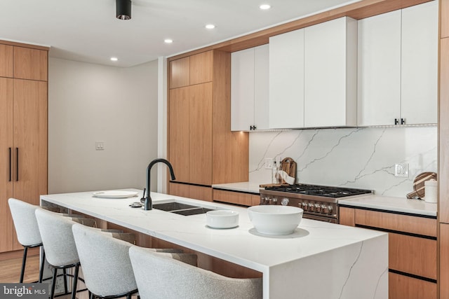 kitchen with tasteful backsplash, a kitchen island with sink, and white cabinets