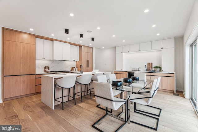 kitchen with white cabinets, light hardwood / wood-style floors, tasteful backsplash, and a kitchen island with sink