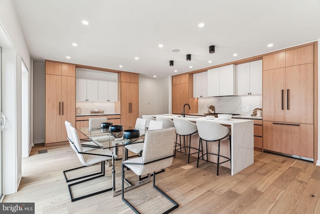 kitchen featuring a kitchen bar, light wood-type flooring, tasteful backsplash, a kitchen island with sink, and white cabinets