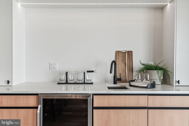 bar with light stone counters, light brown cabinetry, sink, and wine cooler