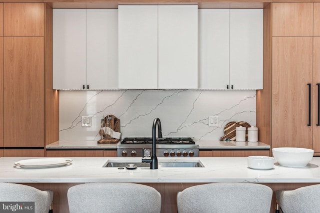 kitchen with a kitchen breakfast bar, decorative backsplash, white cabinetry, and light stone counters