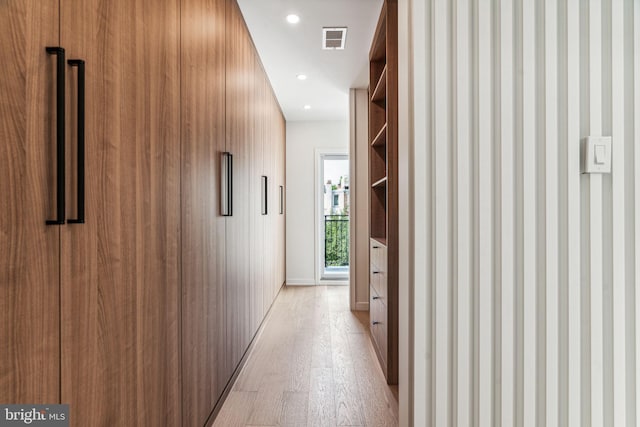 hallway featuring built in shelves, light wood-type flooring, and wood walls