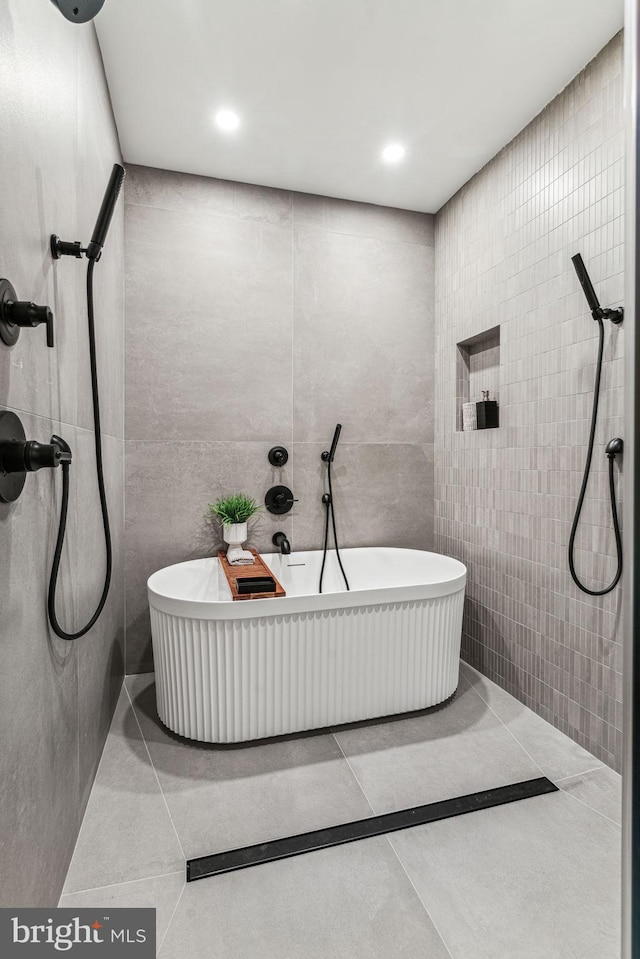 bathroom featuring tile patterned flooring, a bath, and tile walls