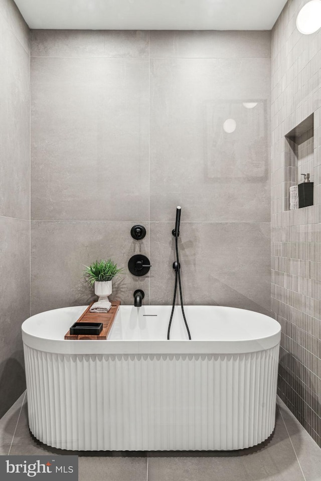 bathroom with tile patterned flooring, a bath, and tile walls