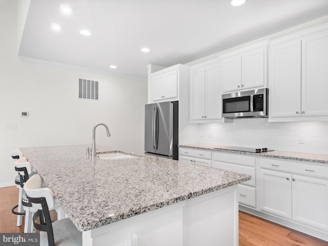 kitchen with white cabinetry, light hardwood / wood-style flooring, a center island with sink, and stainless steel appliances