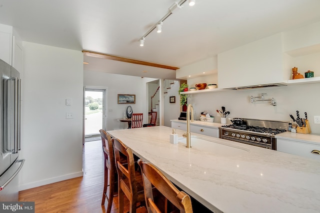 kitchen featuring stainless steel range, light wood finished floors, open shelves, white cabinetry, and a sink