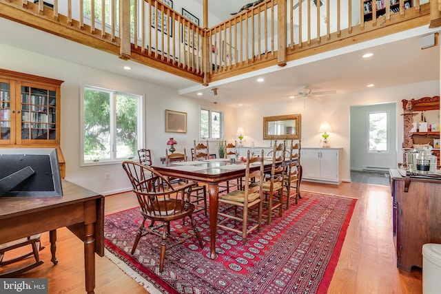 dining space with light hardwood / wood-style flooring, a wealth of natural light, ceiling fan, and a high ceiling