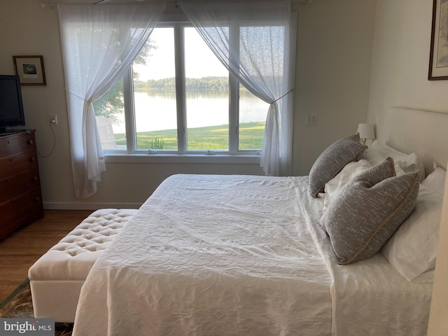 bedroom with multiple windows, hardwood / wood-style floors, and a water view