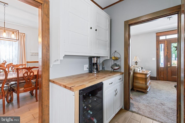 kitchen with beverage cooler, white cabinetry, hanging light fixtures, and wood counters