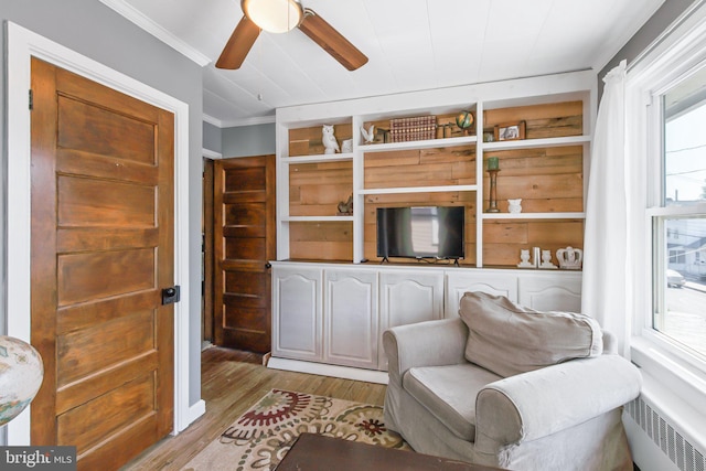 living area with crown molding, wood-type flooring, radiator heating unit, and ceiling fan