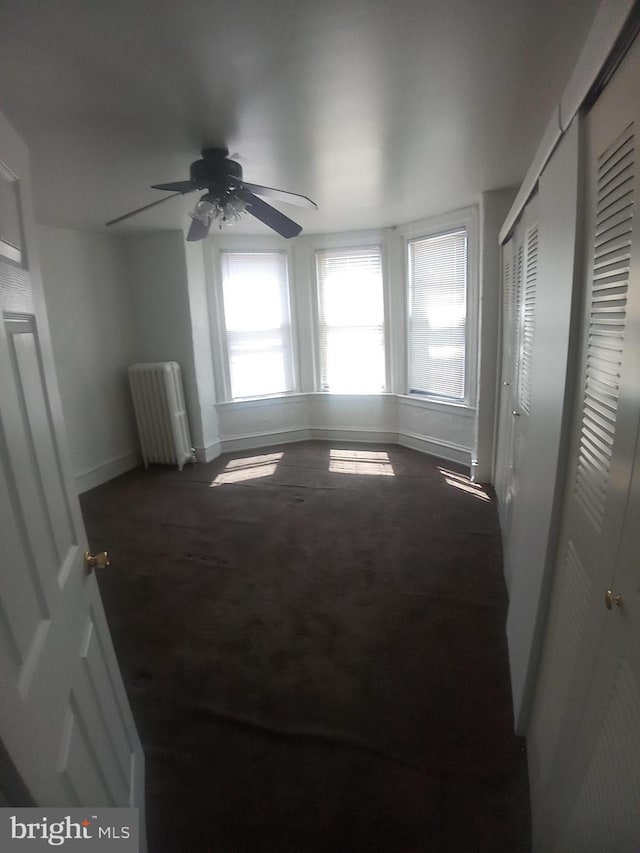 carpeted empty room with radiator and ceiling fan