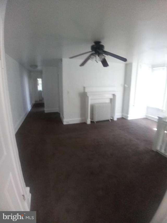 unfurnished living room featuring dark colored carpet, radiator heating unit, a textured ceiling, and ceiling fan