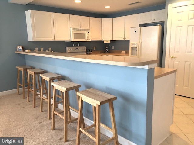 kitchen featuring kitchen peninsula, white appliances, light carpet, a breakfast bar, and white cabinets