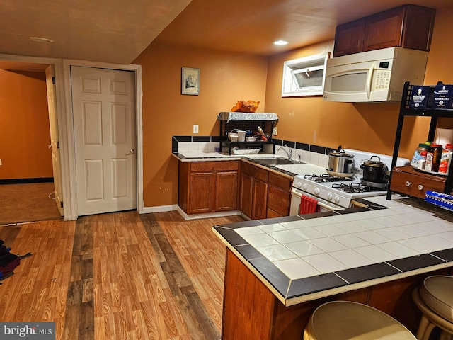 kitchen with tile counters, range with gas cooktop, light wood-type flooring, sink, and a breakfast bar area