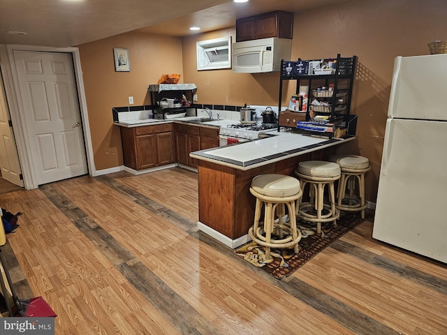 kitchen with white appliances, a kitchen breakfast bar, wood-type flooring, and kitchen peninsula