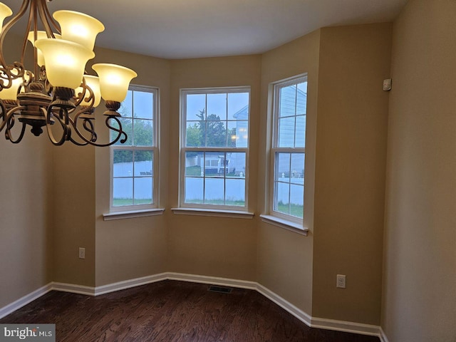 unfurnished room featuring wood-type flooring, plenty of natural light, and an inviting chandelier