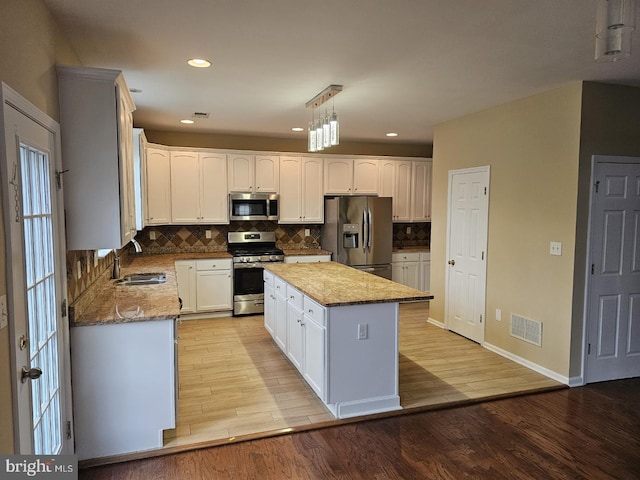 kitchen with light hardwood / wood-style floors, stainless steel appliances, a center island, sink, and white cabinets