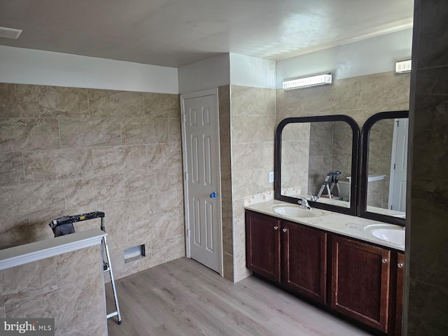 bathroom with tile walls, dual bowl vanity, and hardwood / wood-style floors