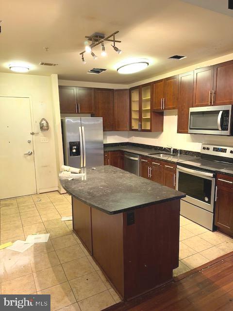 kitchen with light tile floors, a kitchen island, rail lighting, sink, and appliances with stainless steel finishes