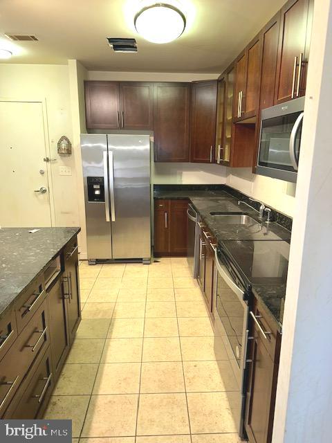 kitchen with dark stone countertops, sink, light tile floors, and appliances with stainless steel finishes